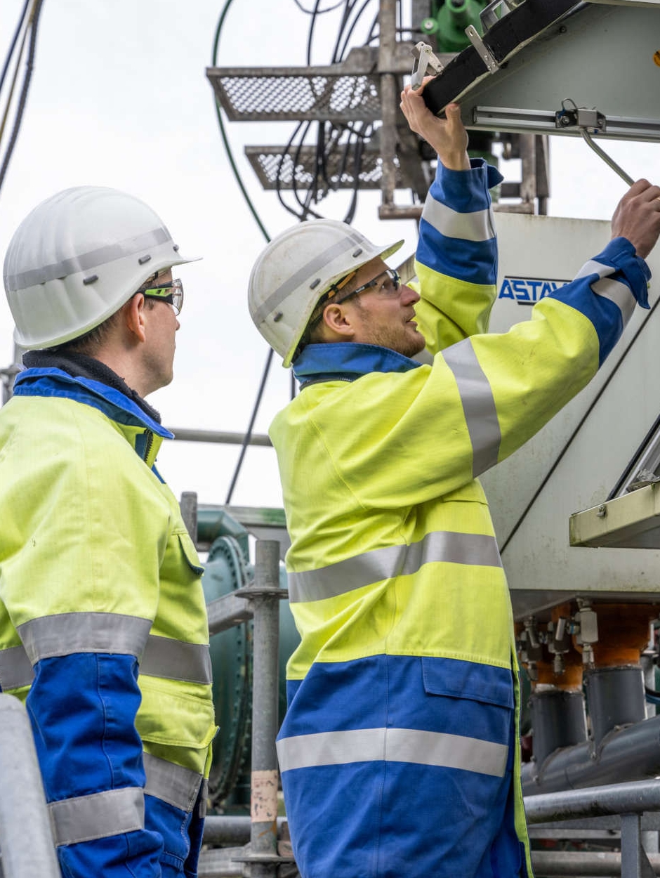 Zwei Ingenieure in Schutzkleidung und weißem Helm sind auf einem Kavernenplatz und lesen den Druck an einem Drucktransmitter ab