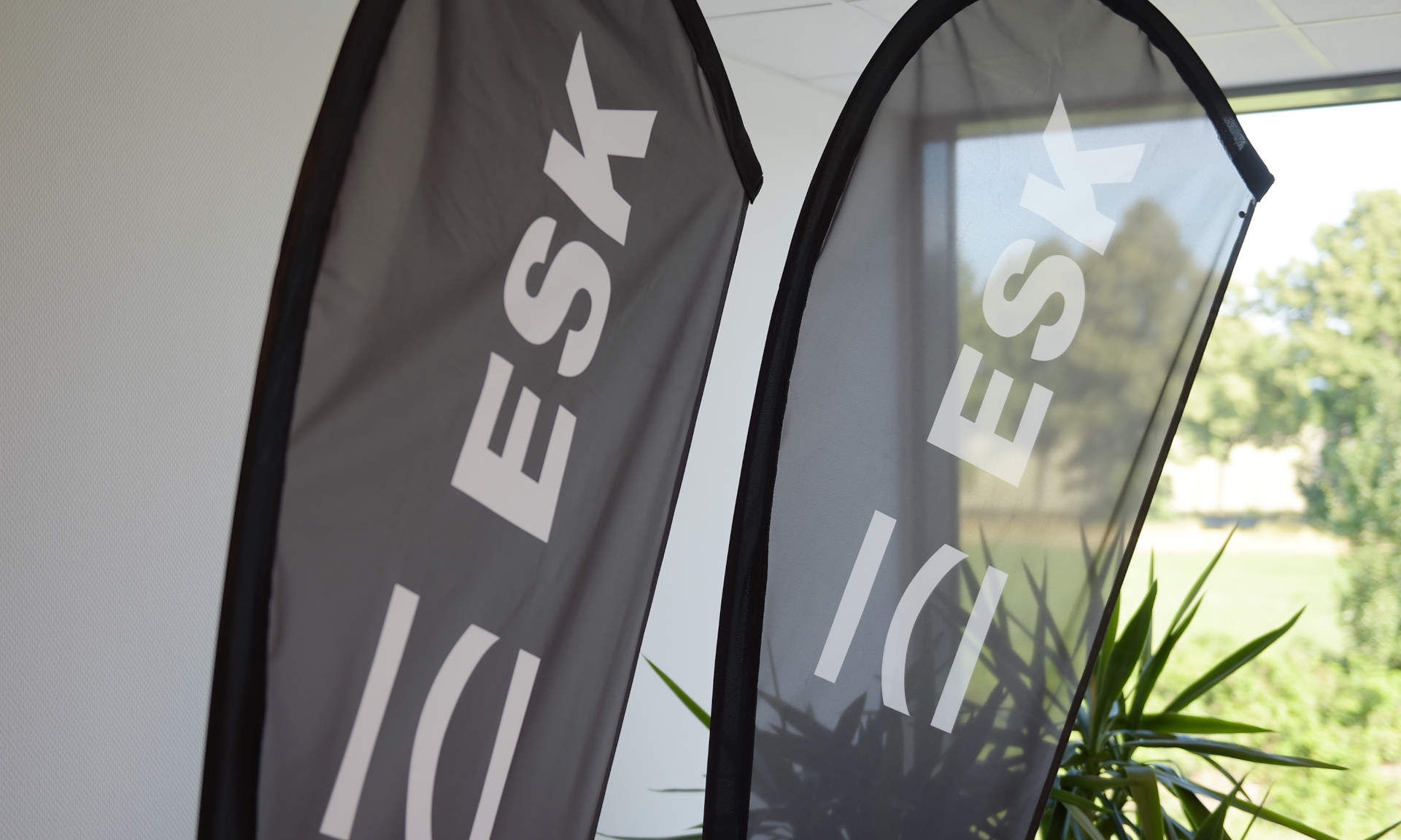Zwei schwarze Beachflags mit Logo der ESK GmbH vor einer Pflanze und einem großen Fenster