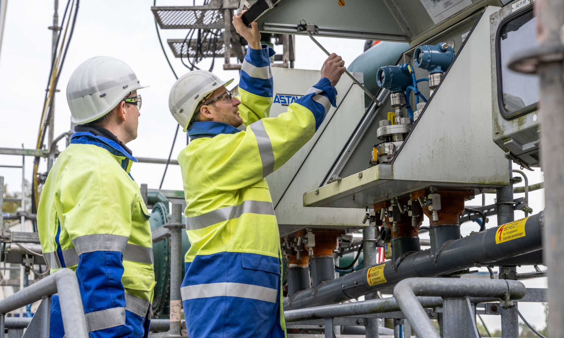 Zwei Ingenieure in Schutzkleidung und weißem Helm sind auf einem Kavernenplatz und lesen den Druck an einem Drucktransmitter ab
