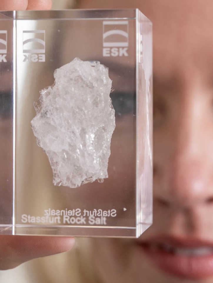 Andrea Wobito hält ein Acrylglas, in dem ein Stück Steinsalz aus Staßfurt eingegossen ist, in die Kamera