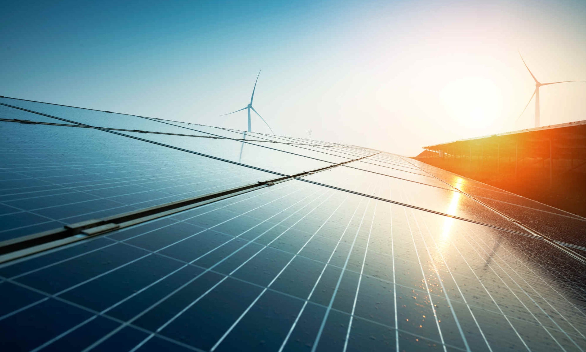 Solar park with wind turbines and a setting sun in the background