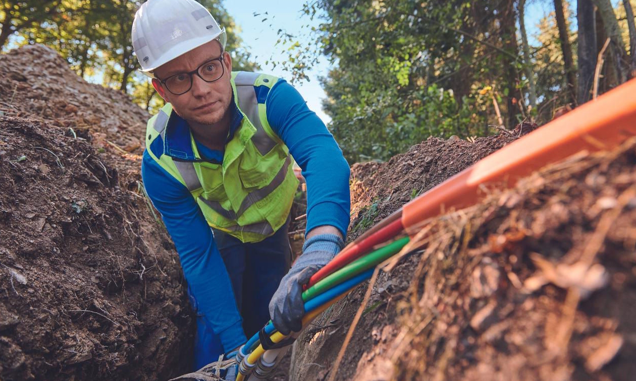 Employee in protective clothing and a white safety helmet laying a multi-core cable in a trench