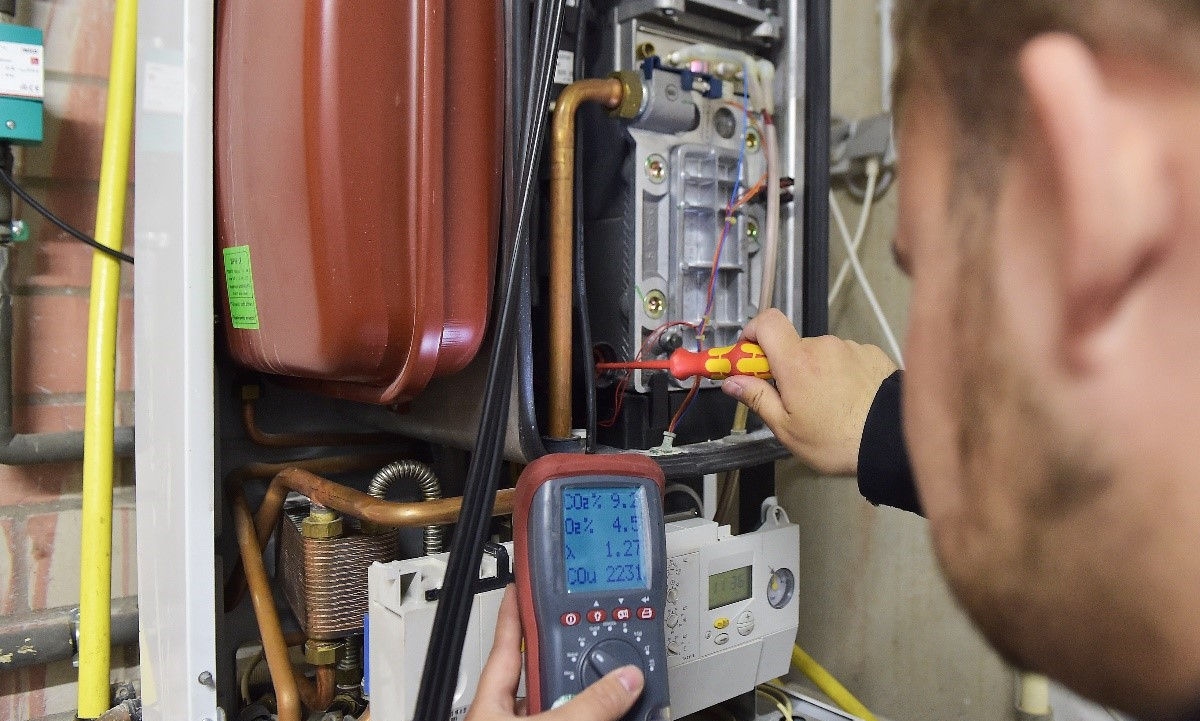 Technician checking a heating system with a multimeter and screwdriver