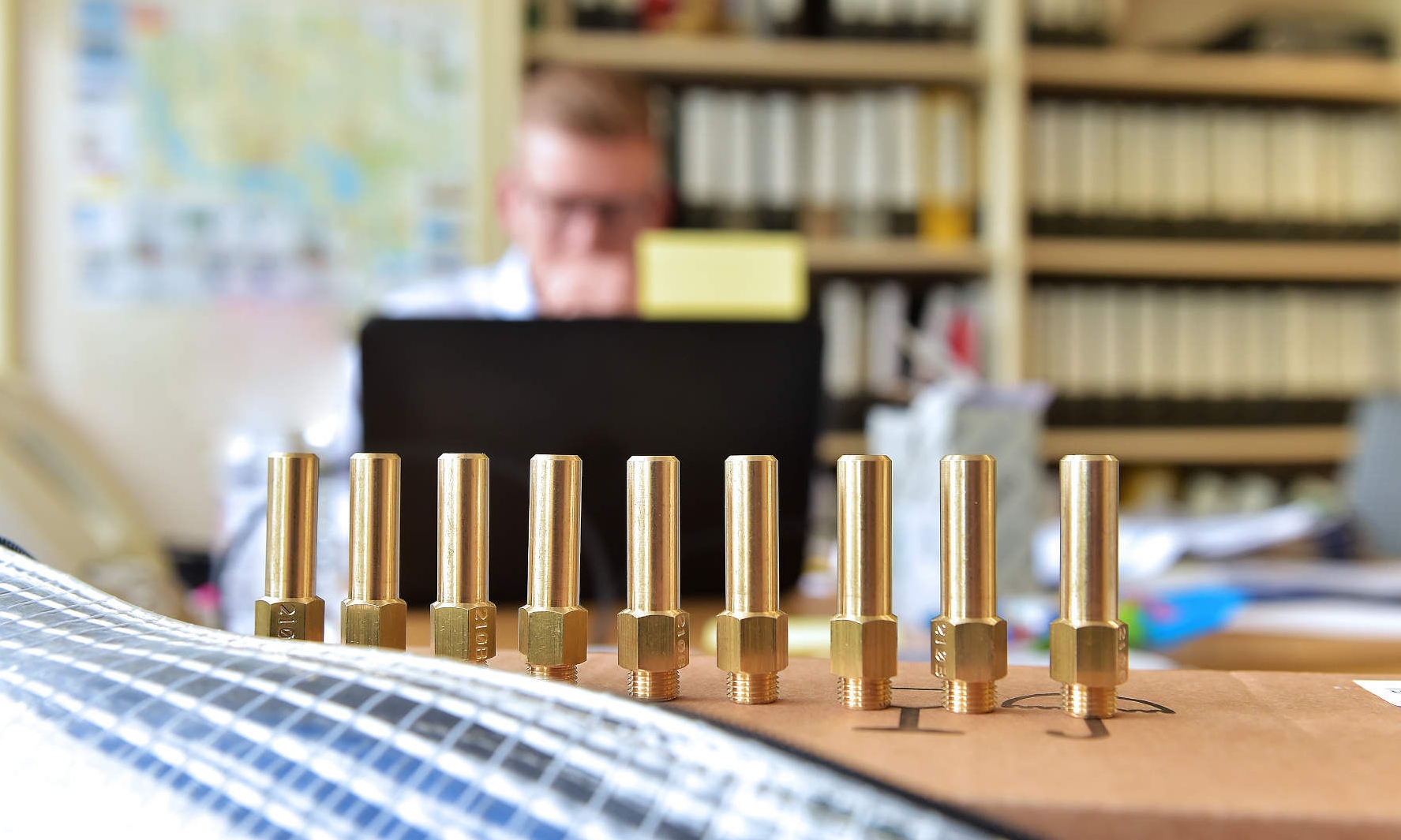 Project engineer sitting at his desk in front of his monitor, with nozzles used for the market area conversion from L-gas to H-gas lined up in the foreground
