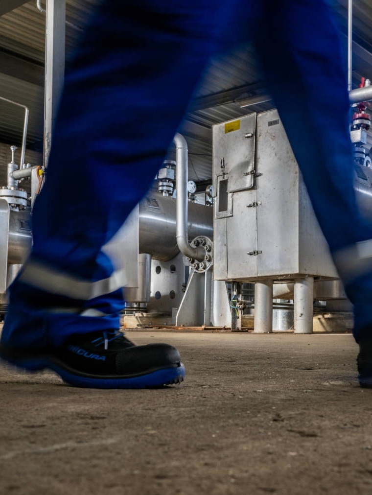 Ein Mensch in Arbeitskleidung, nur die Beine sind sichtbar, läuft auf der Methanol-Anlage eines Untertagegasspeichers entlang