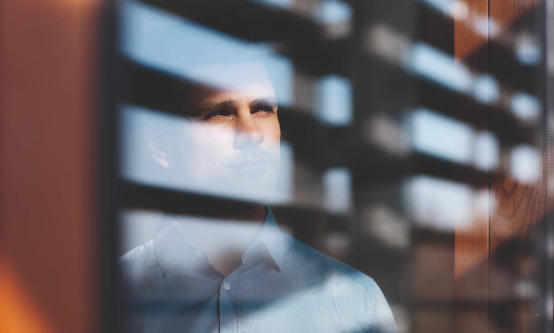 Man looking thoughtfully through window blinds 