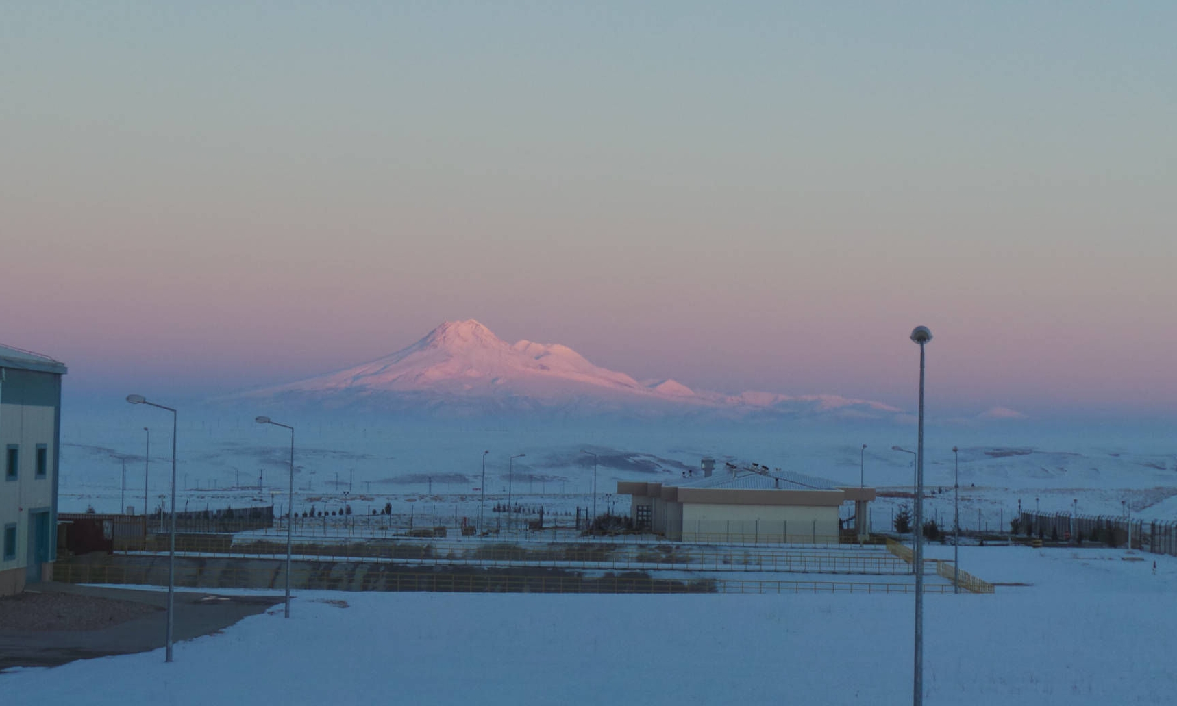 View over a surface facility of a cavern site with a snow-covered landscape and mountain in the background in evening light