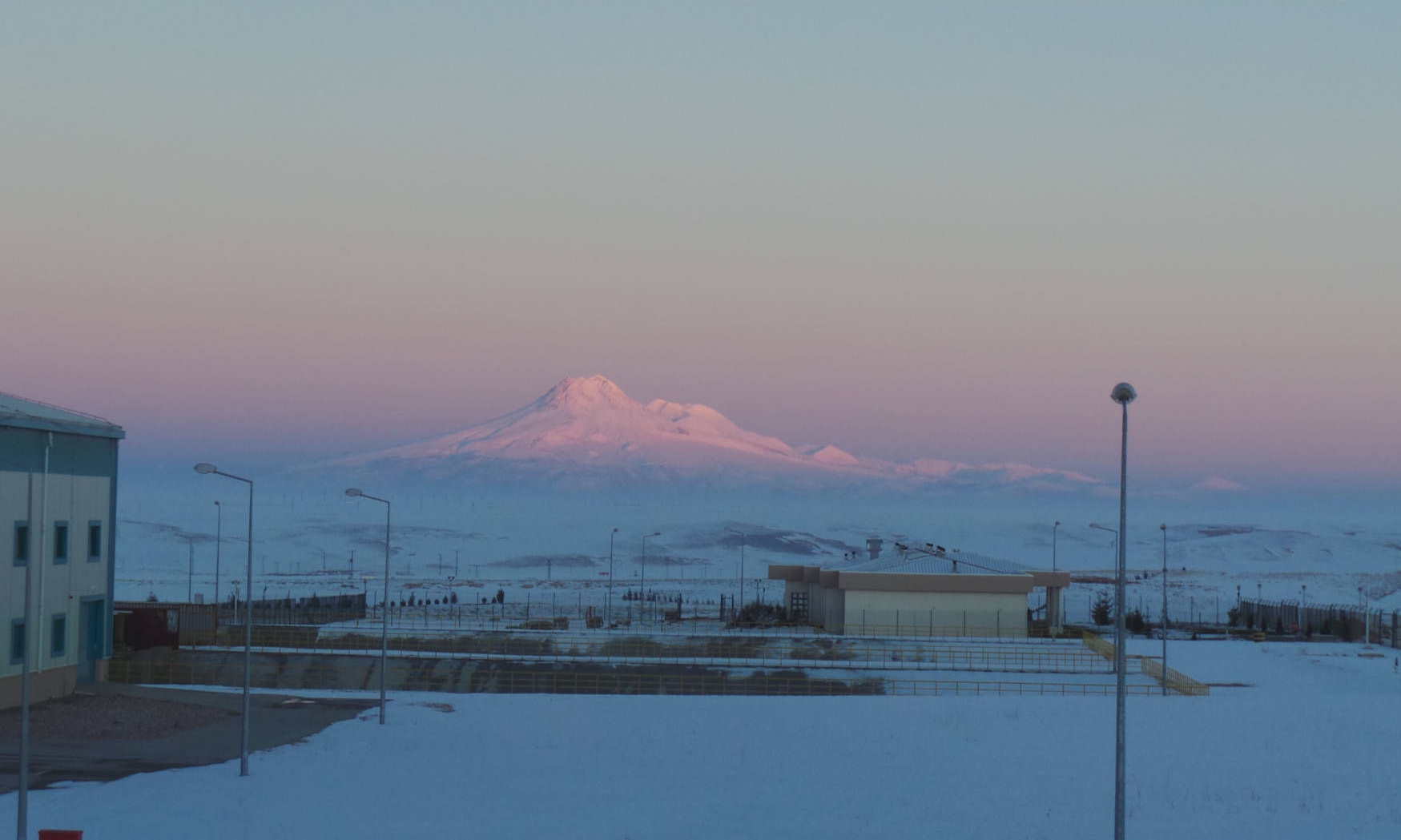 View over a surface facility of a cavern site with a snow-covered landscape and mountain in the background in evening light