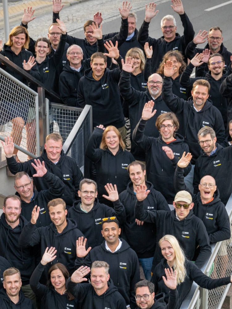 Waving team of ESK GmbH in black sweaters on a staircase